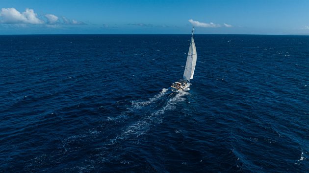An aerial of a yacht sailing in the distance with blue skies