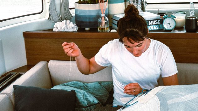 Saskia sewing some fabrin in the cabin. She is wearing a t-shirt and her hair in a bun.