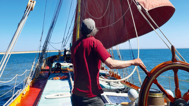Conning the Thames Barge Blue Mermaid into an anchorage – the wheel in one hand, mainsheet in the other while the mate is forward preparing the anchor. The head of the topsail has been dropped, but the sheet not yet run in. The vessel can be slowed or speeded up as needed while choosing the spot to let go the anchor – all by a crew of two.